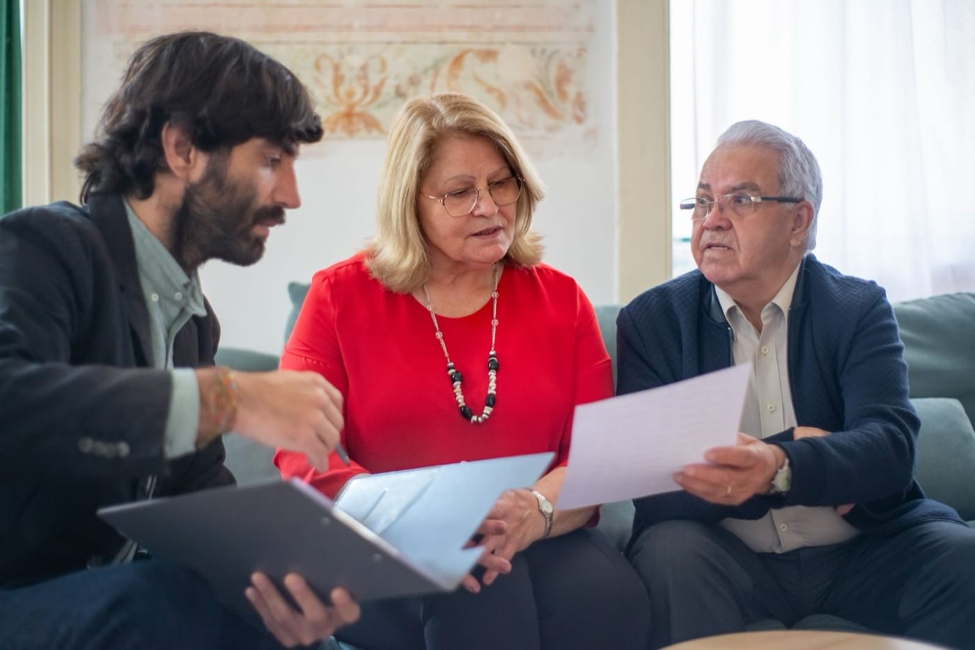 Asesor explicando la documentación de un préstamo a una pareja mayor en el salón de su casa